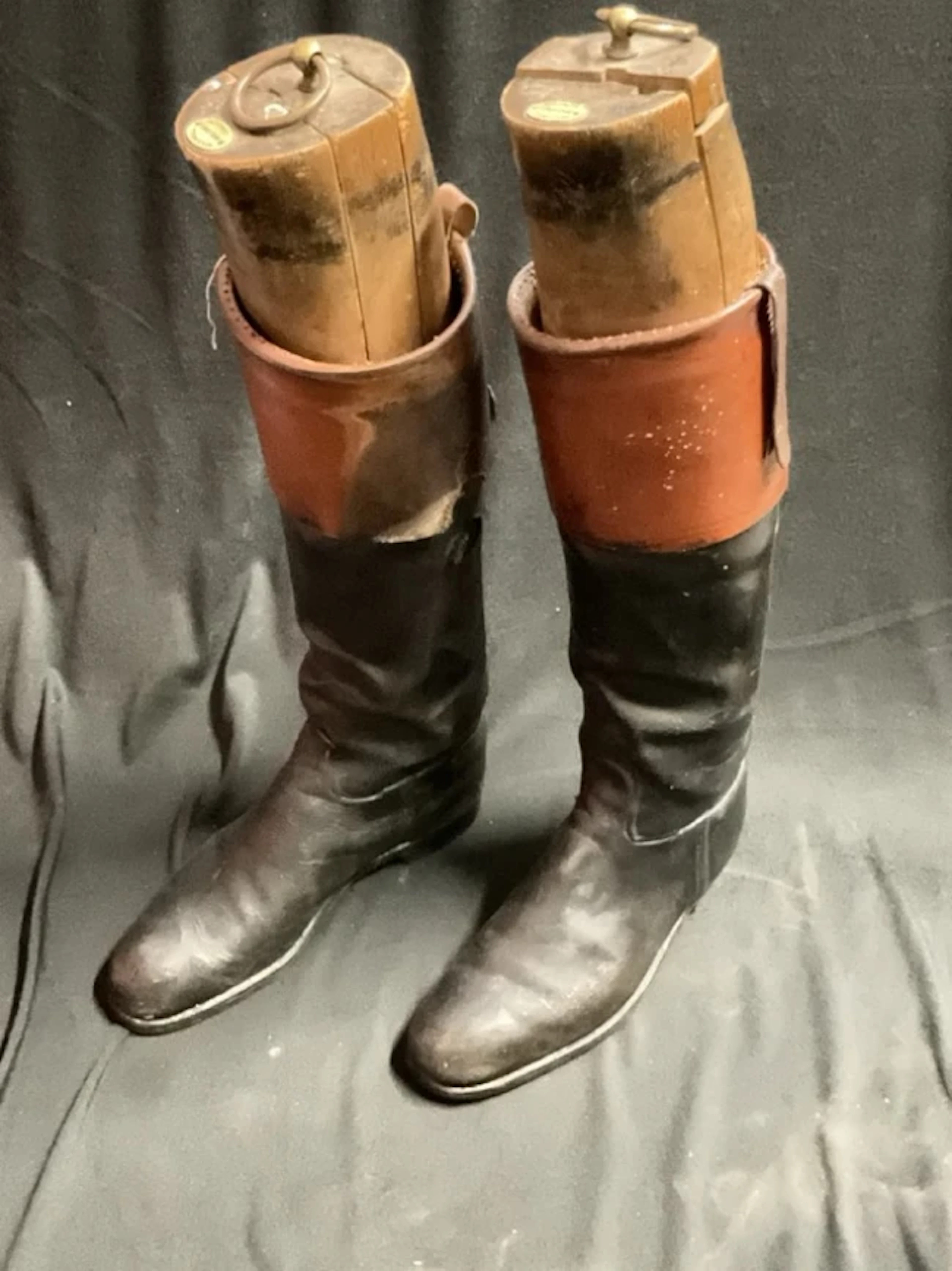 A pair of black and tan riding boots with brass ring handled beech