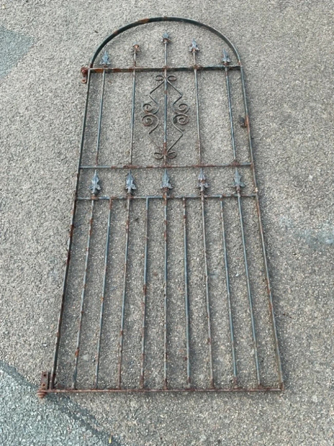 An arched wrought iron garden gate with spear finials to spindles