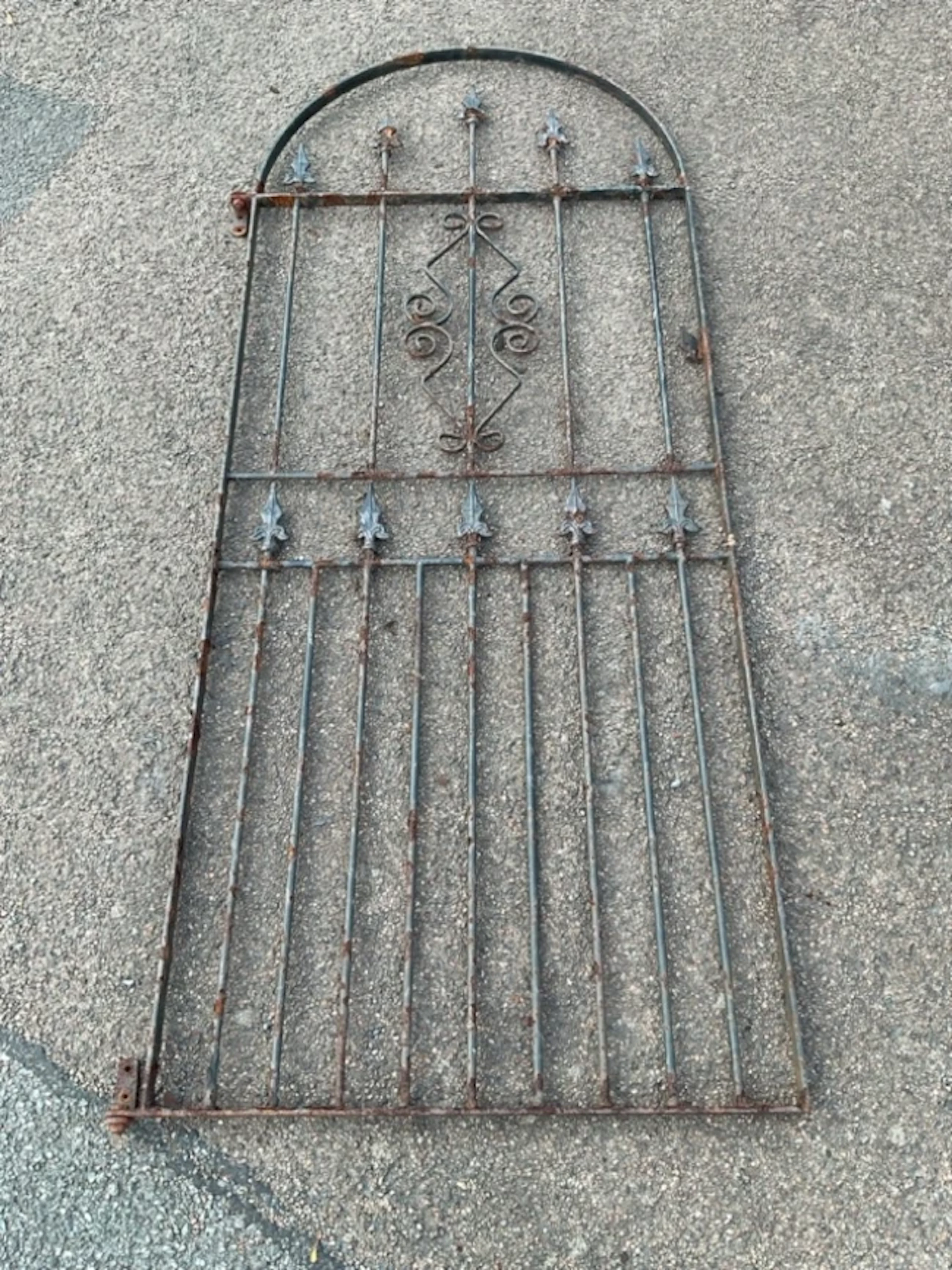 An arched wrought iron garden gate with spear finials to spindles
