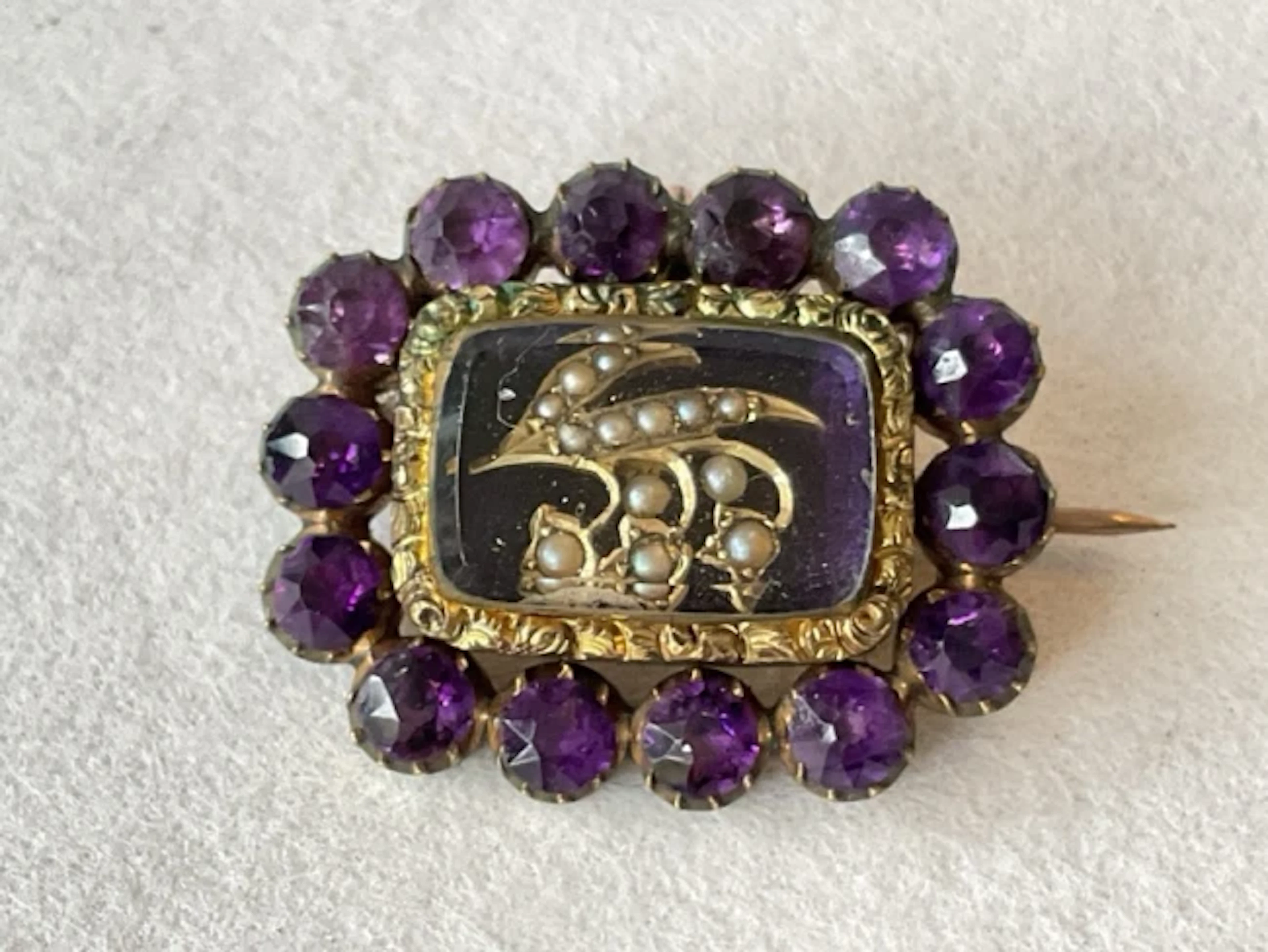 A Victorian gold memorial brooch with amethysts, framing a seed pearl