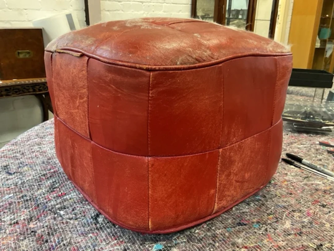 A leather upholstered square pooffe with patchwork panels, having