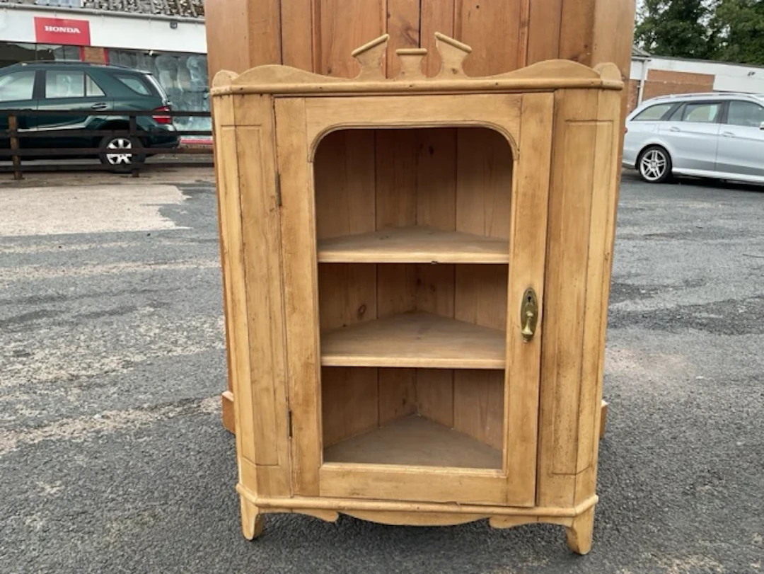 A pine hanging corner cabinet with shaped crest above a rounded panelled