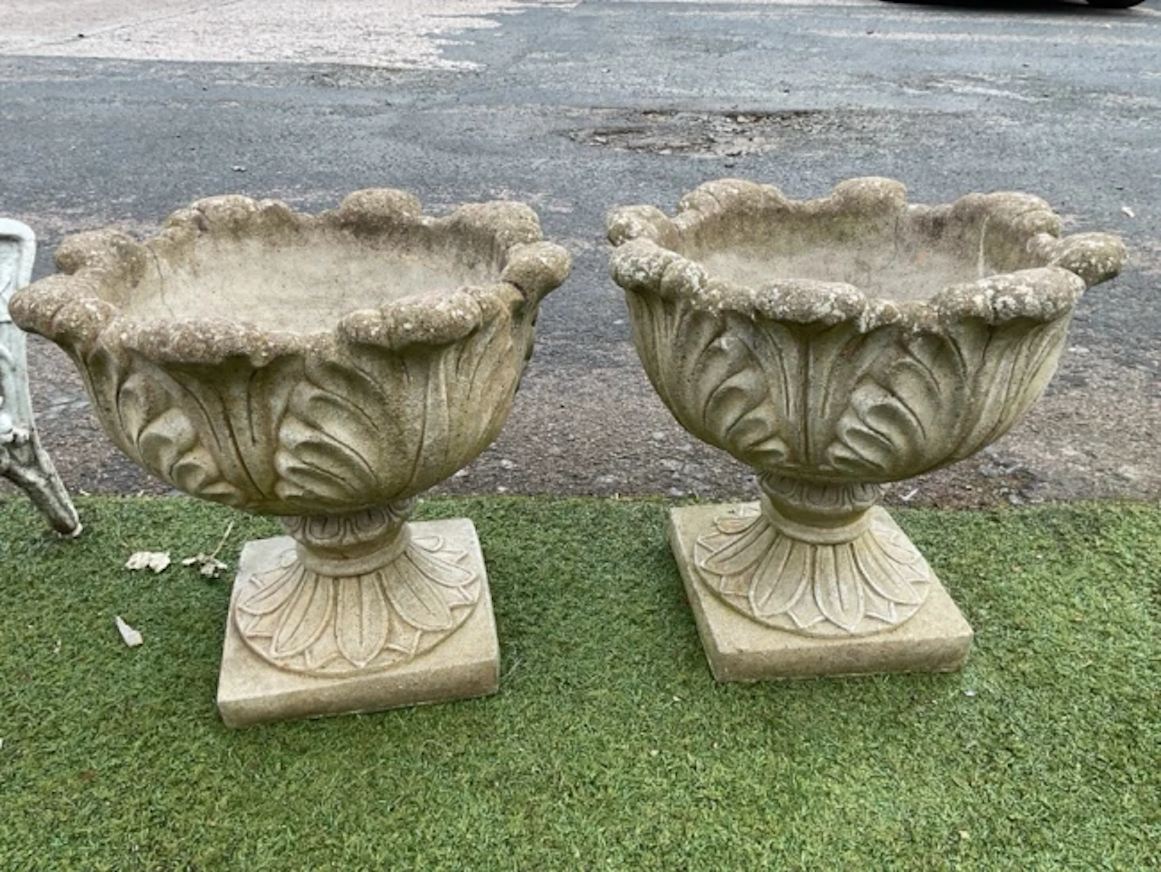 A pair of composition stone garden urns with leaf moulded bowls and