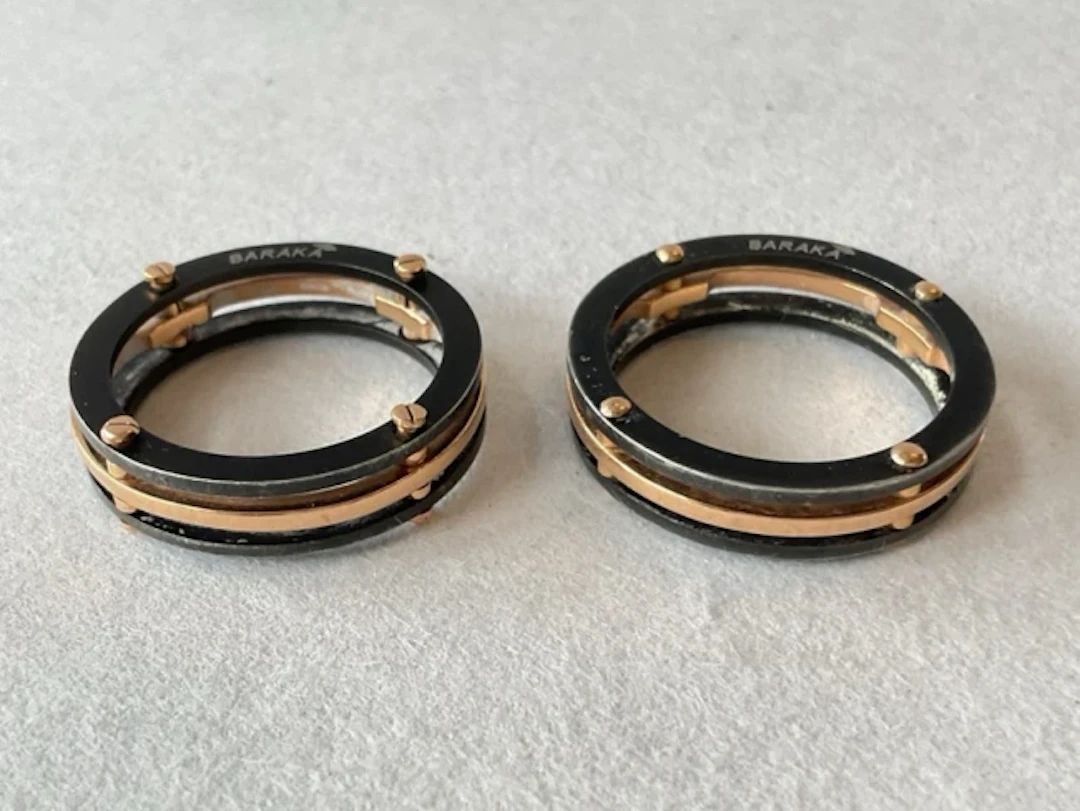 A pair of Baraka black steel and 18ct gold rings, the triple bands