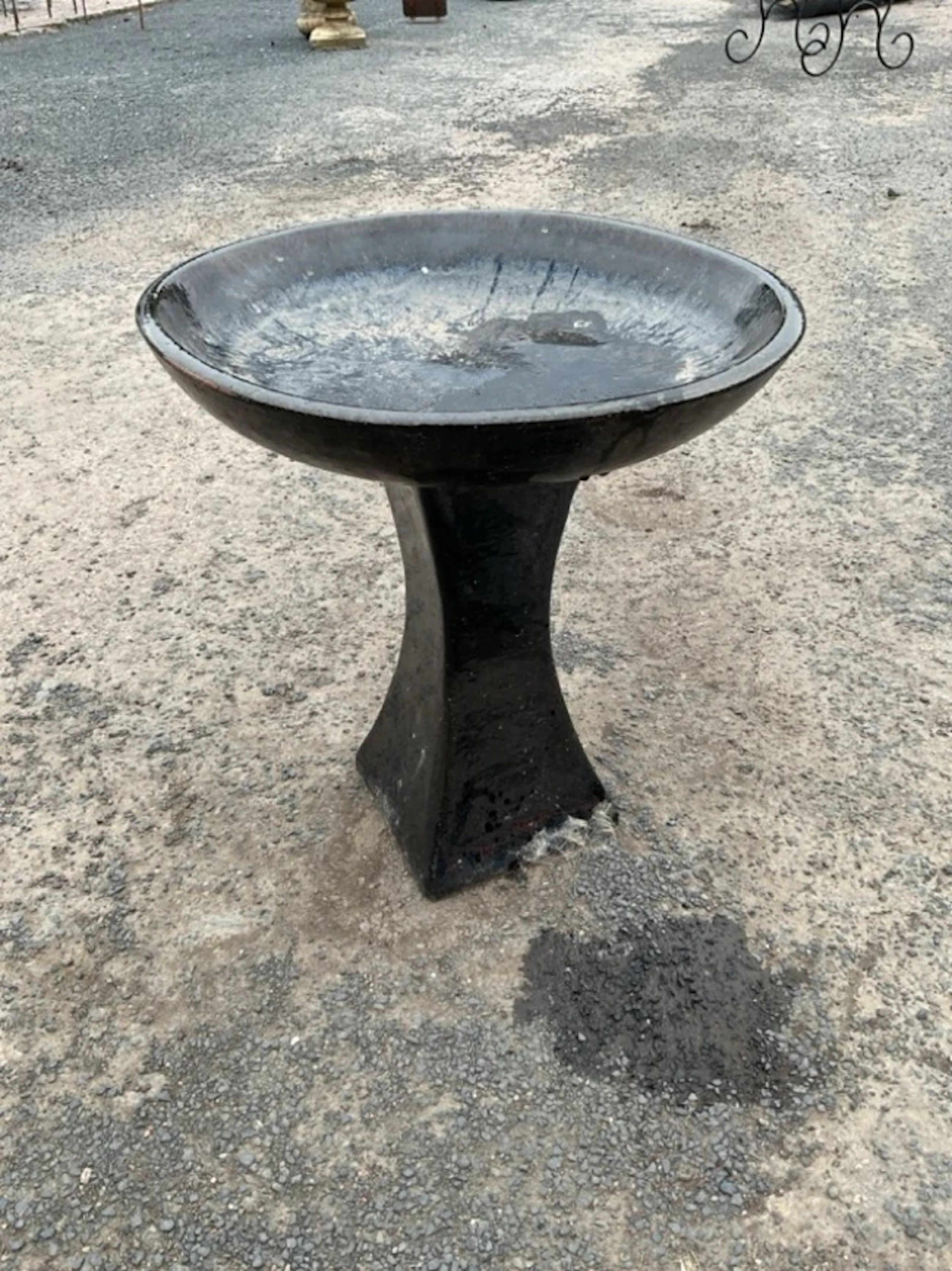 A black glazed terracotta garden birdbath with circular bowl on square