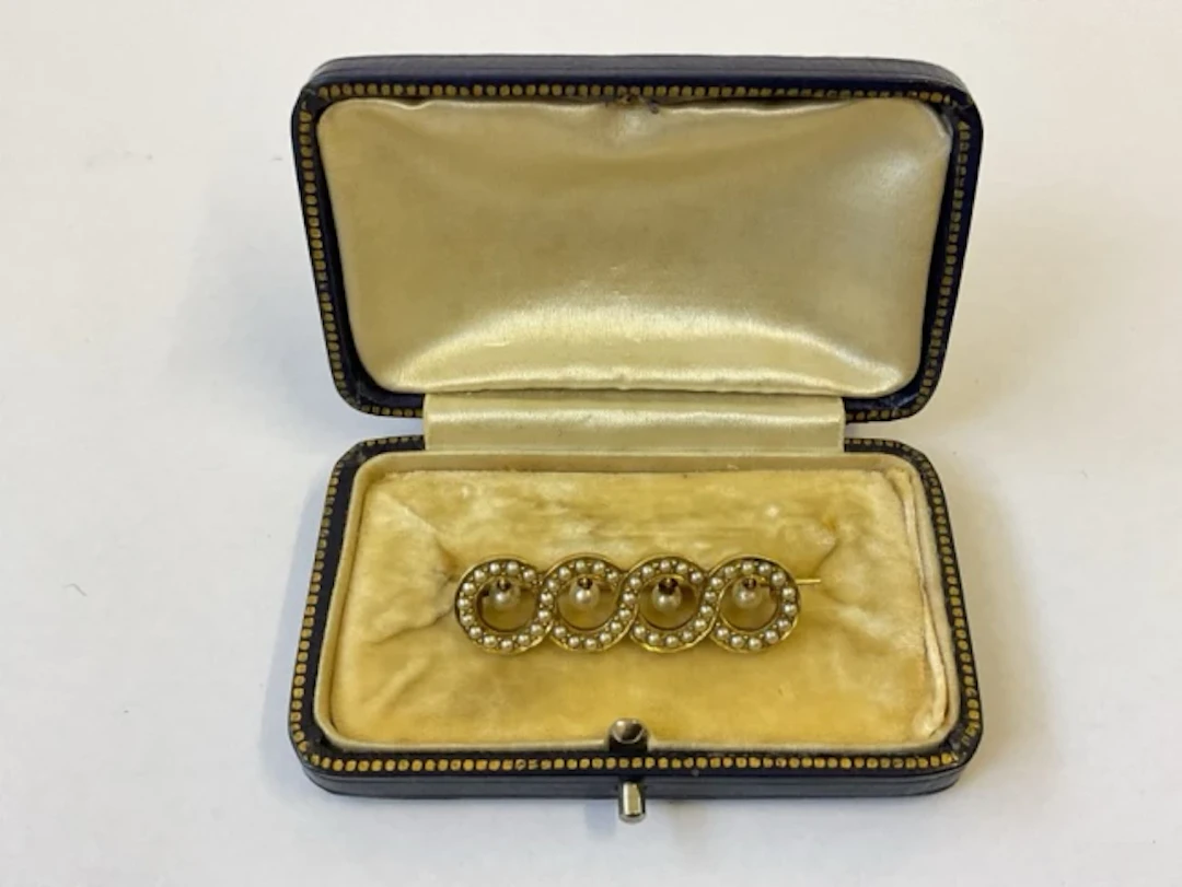 An antique boxed 15ct gold brooch set with seed pearls on interlaced