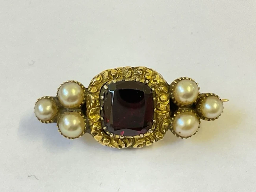 A Georgian gold memorial brooch with cushion cut garnet in scrolled