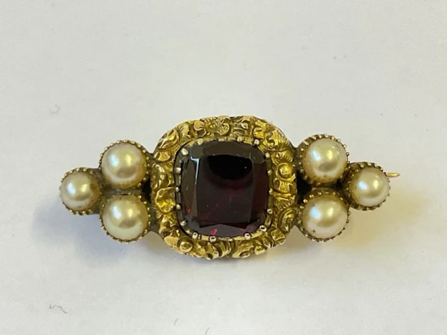 A Georgian gold memorial brooch with cushion cut garnet in scrolled