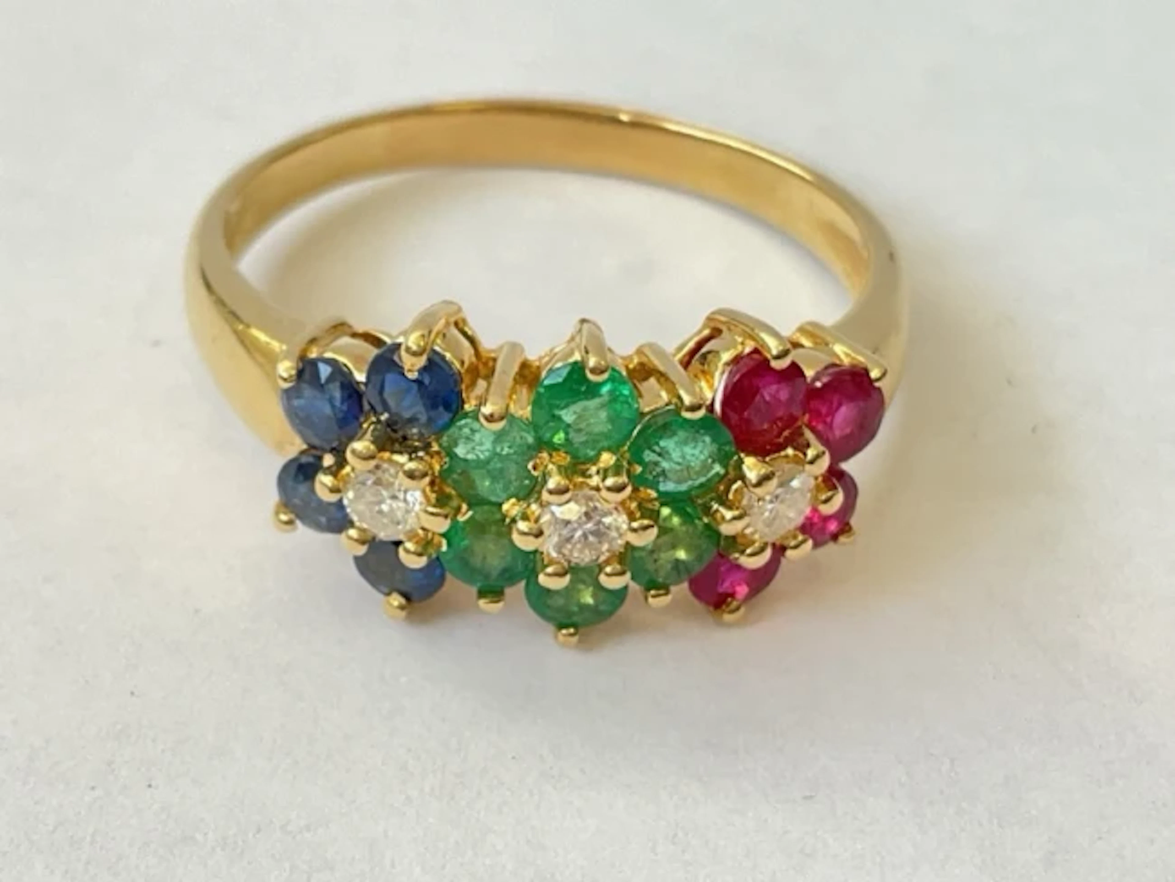 An 18ct gold emerald, ruby & sapphire cluster ring with trio of diamonds