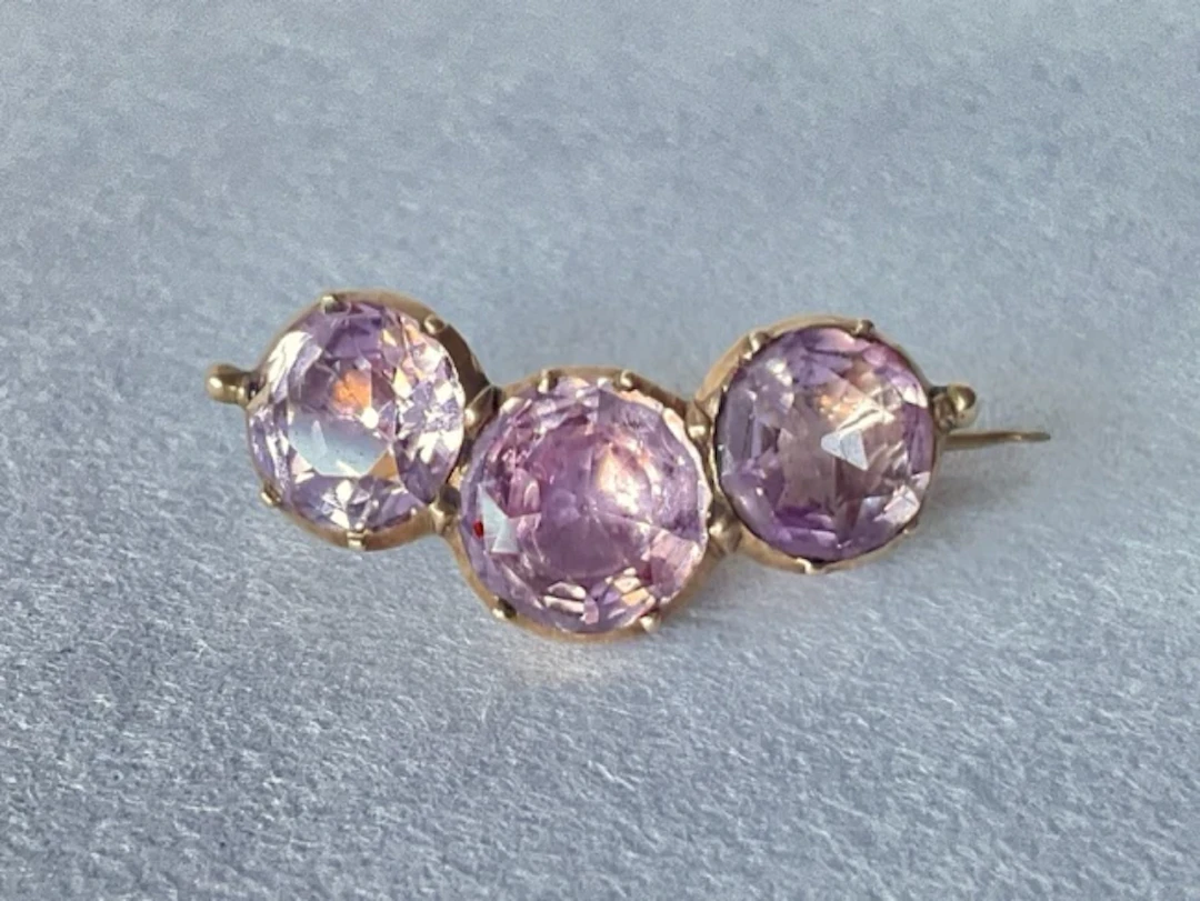 An antique gold brooch set with a trio of circular cut amethysts. (1in)