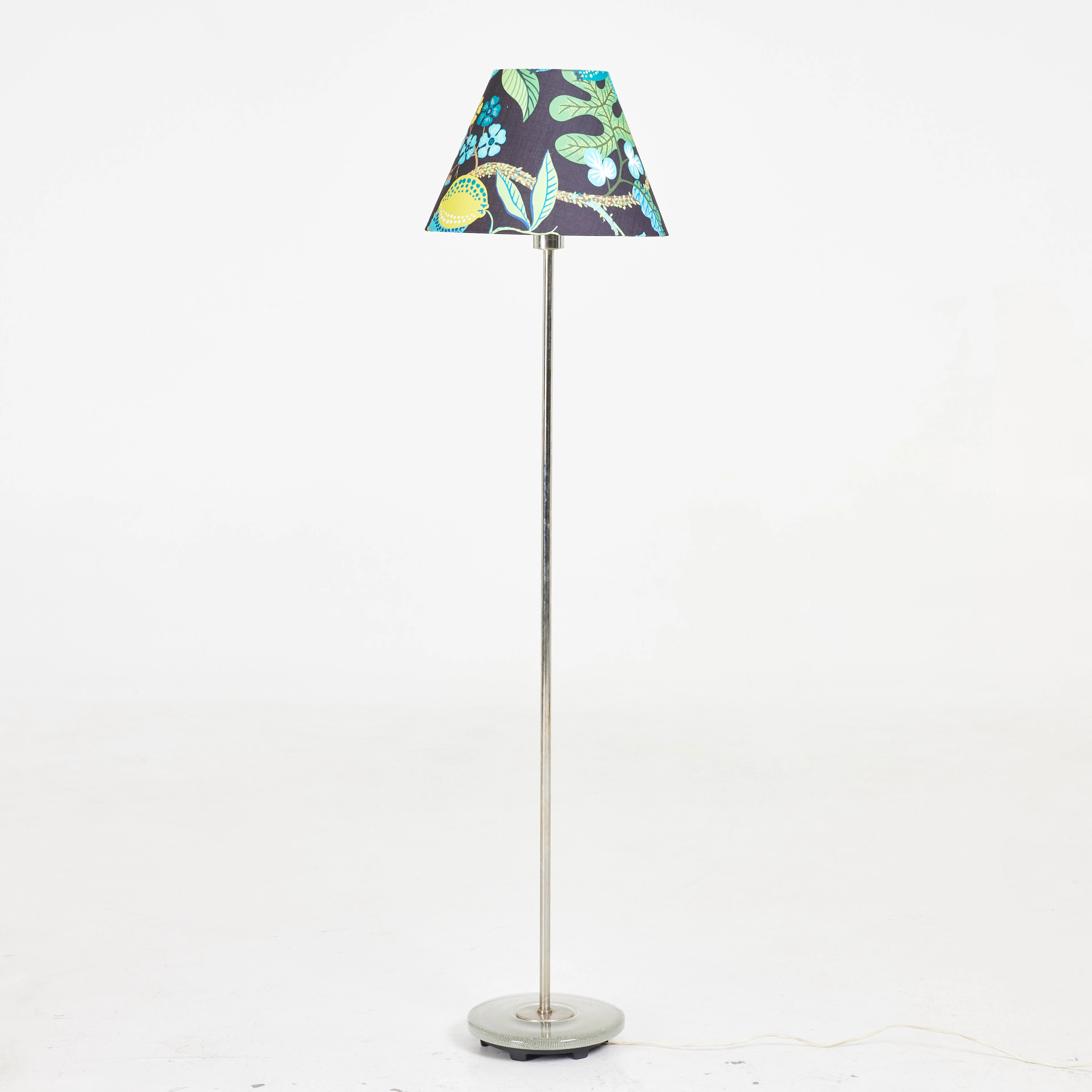 GOLVLAMPA. modell 15704, lampfot i glas och vitmetall, skärm i textil