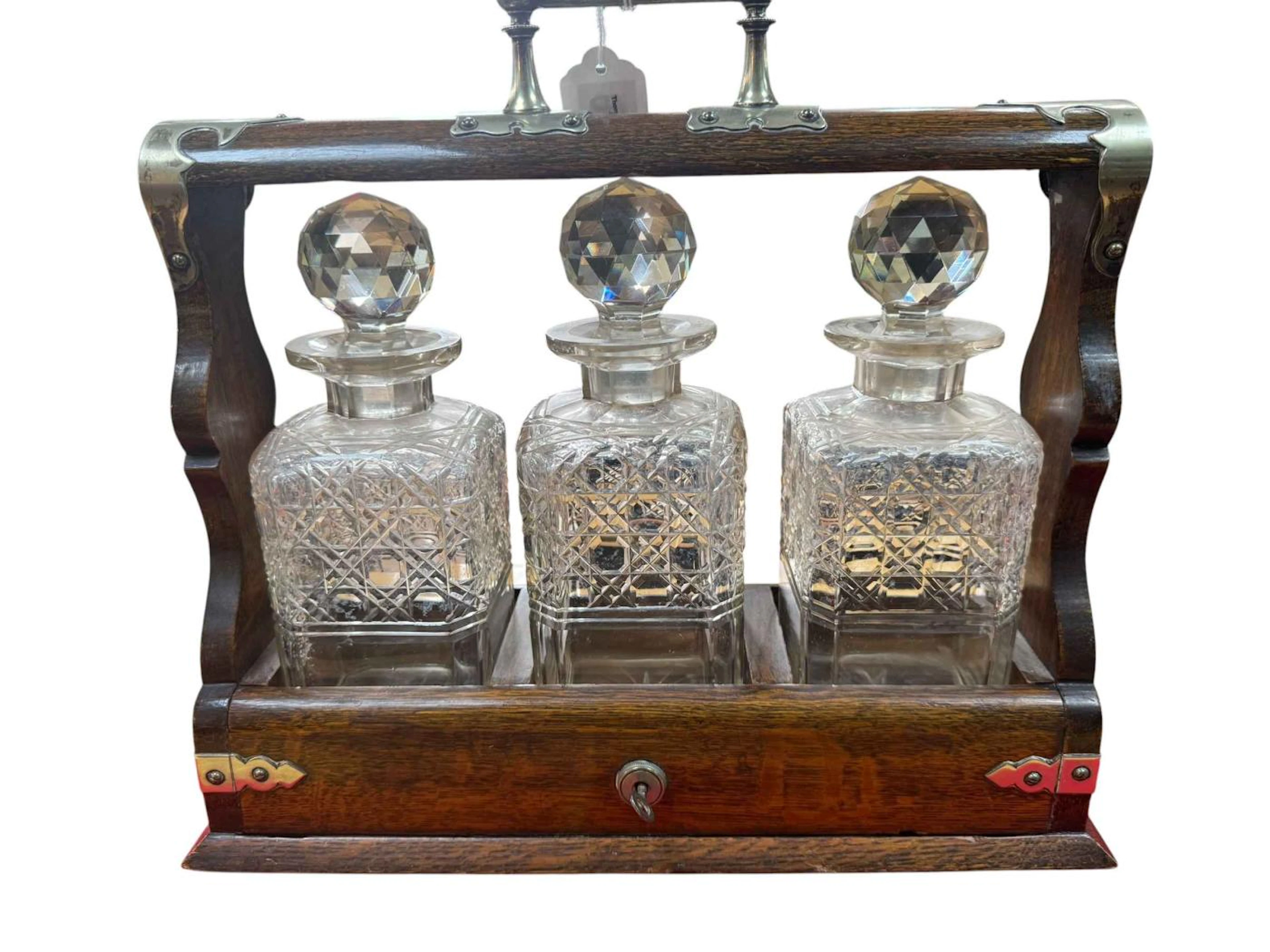 Antique oak and metal three decanter tantalus holding three cut crystal