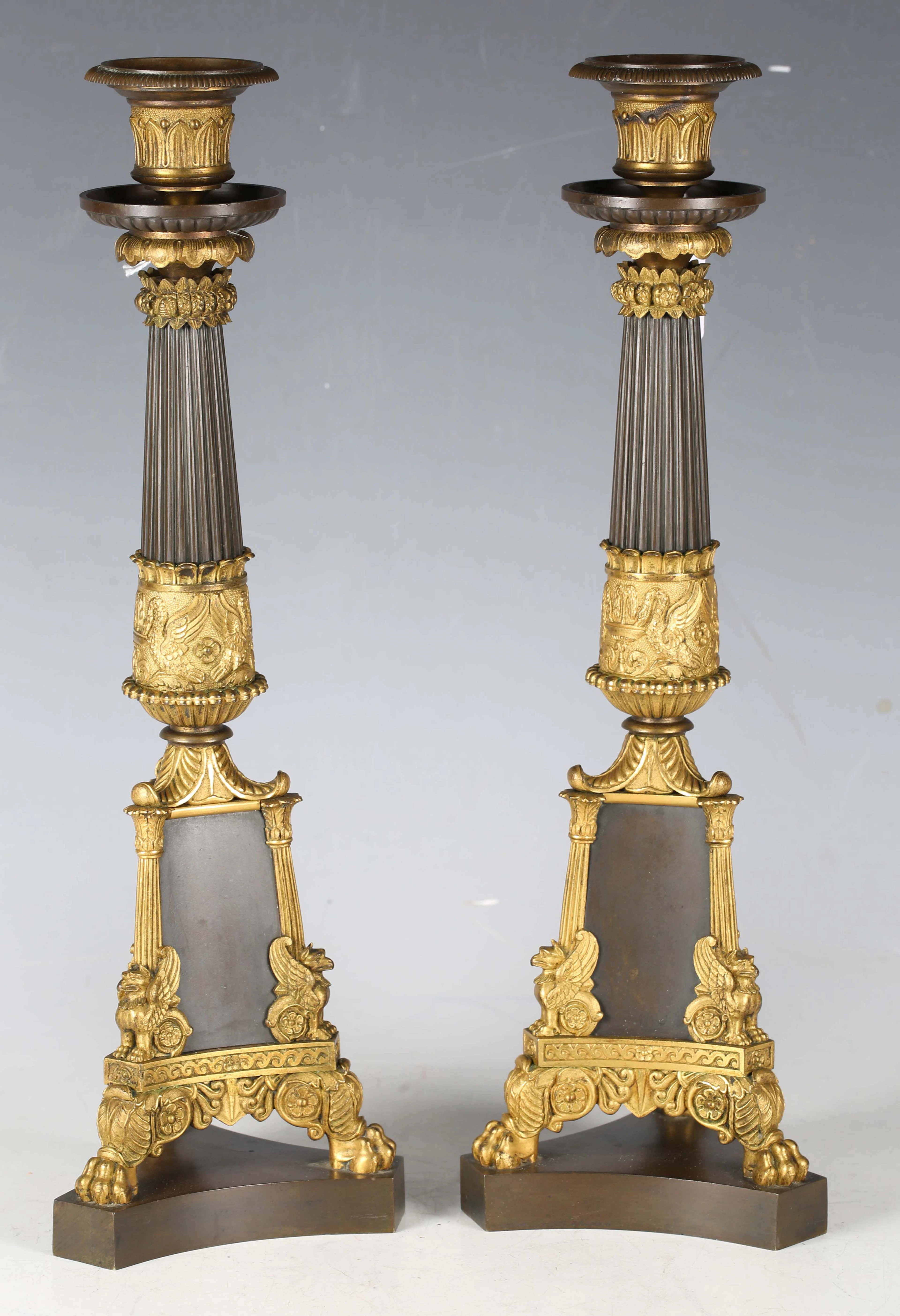A pair of French Empire cast ormolu and brown patinated bronze candlesticks
