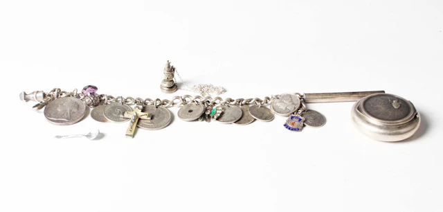 A silver curblink charm bracelet, hung with various coins and charms