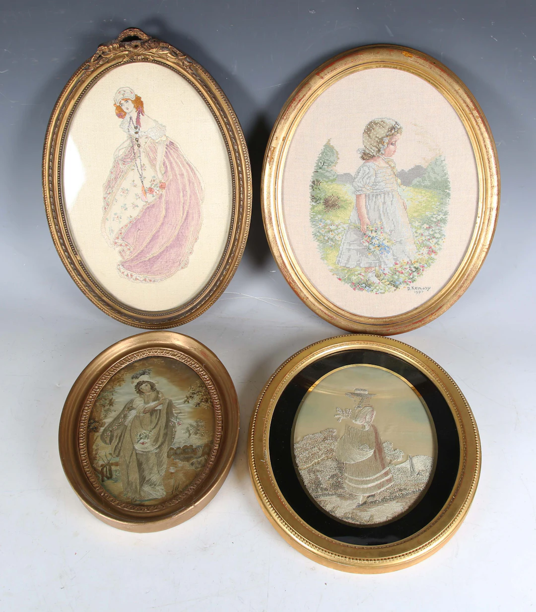 A Regency oval silkwork of a lady walking through a garden, 23cm x