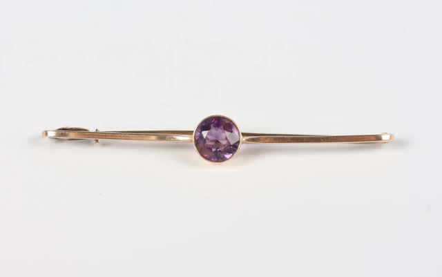 A gold bar brooch, collet set with a circular cut amethyst at the