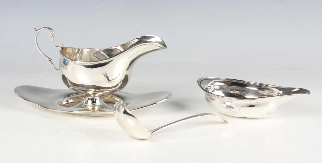 A George V silver sauceboat with foliate-capped scroll handle and
