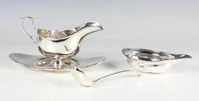 A George V silver sauceboat with foliate-capped scroll handle and