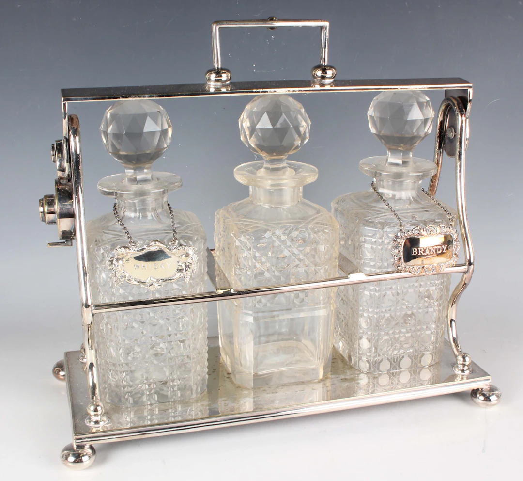 A plated three-bottle tantalus with locking mechanism, on bun feet