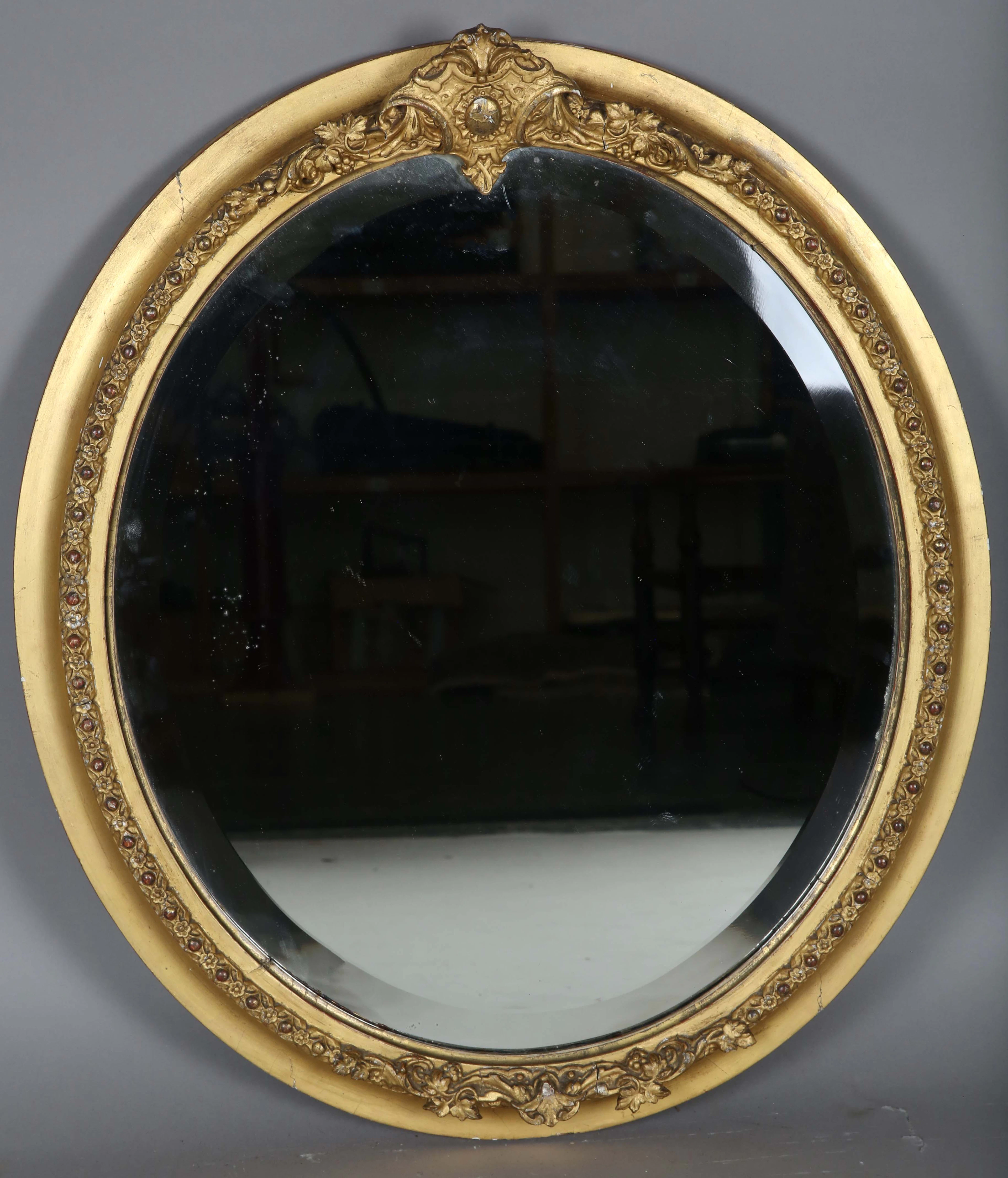 A late Victorian gilt gesso oval wall mirror, the deep bevelled plate