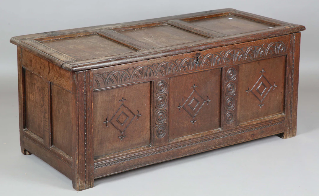 An early 18th century oak panelled coffer, the front with later carved