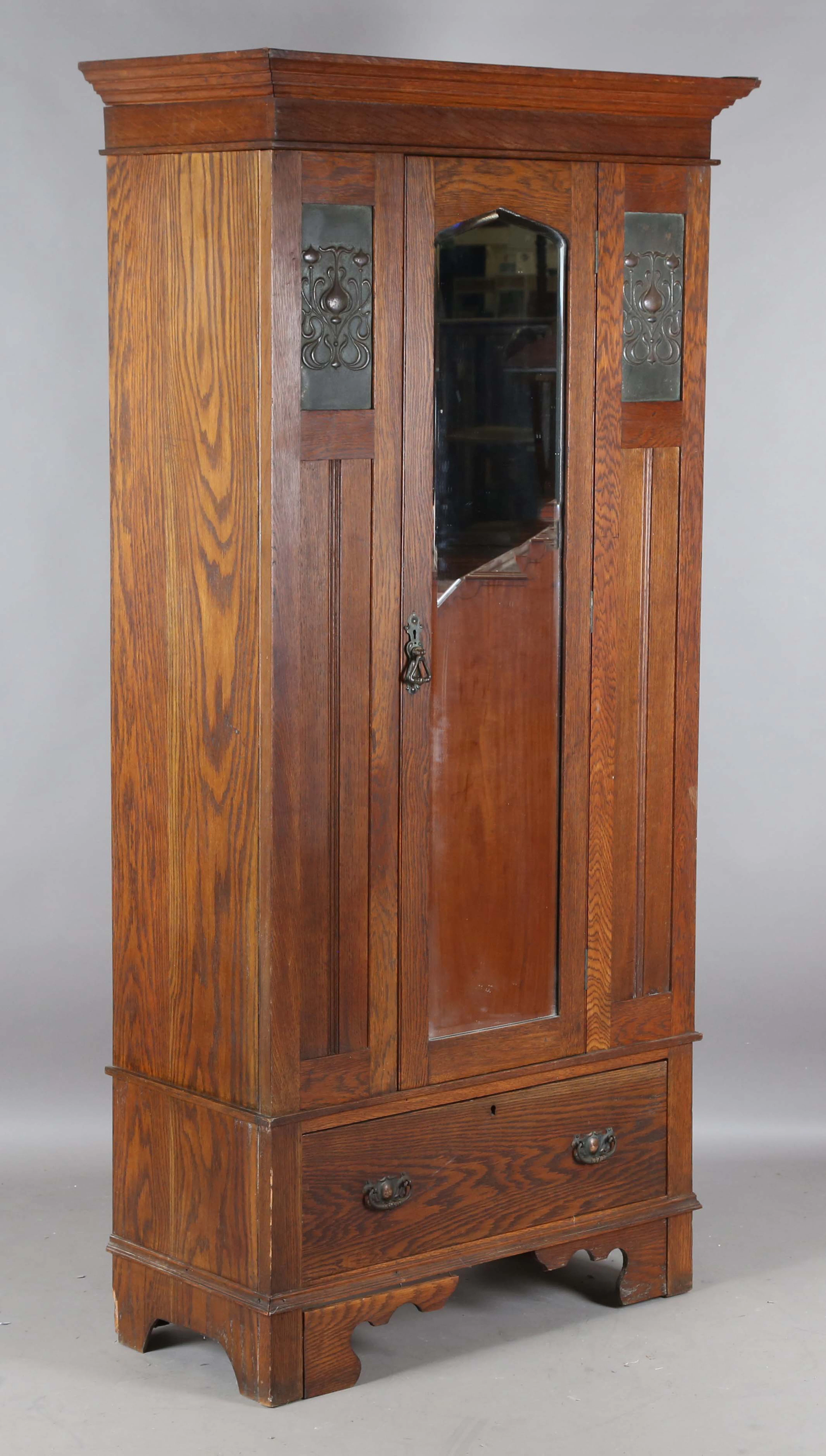 An Edwardian Arts and Crafts oak wardrobe, inset with two pressed
