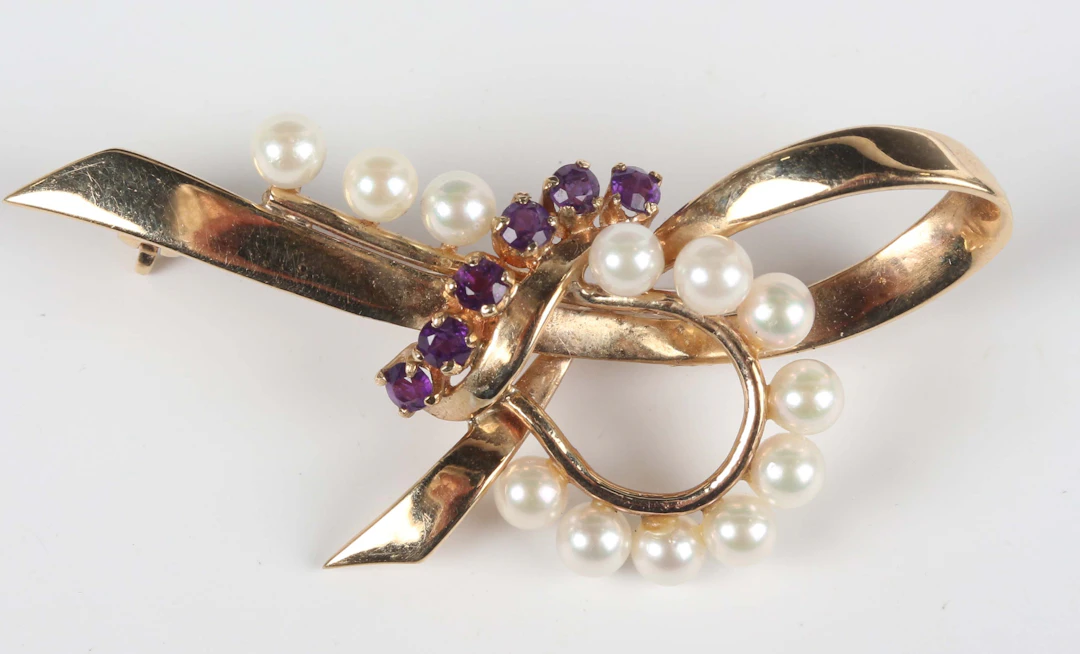A 9ct gold, amethyst and cultured pearl brooch of stylized tied bow
