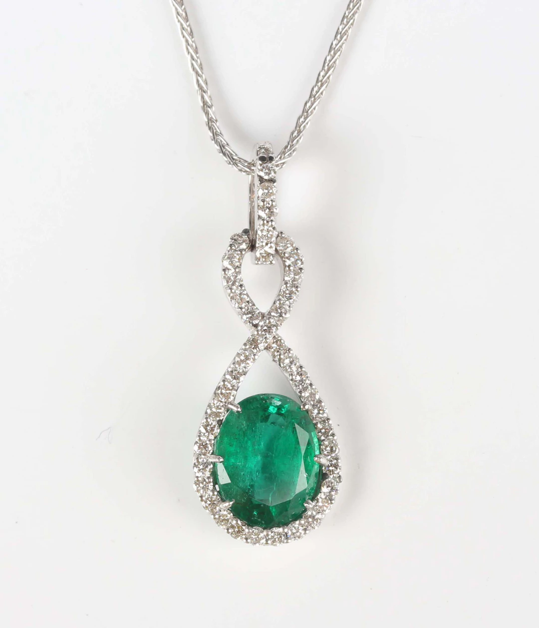 A white gold, emerald and diamond pendant, claw set with the oval