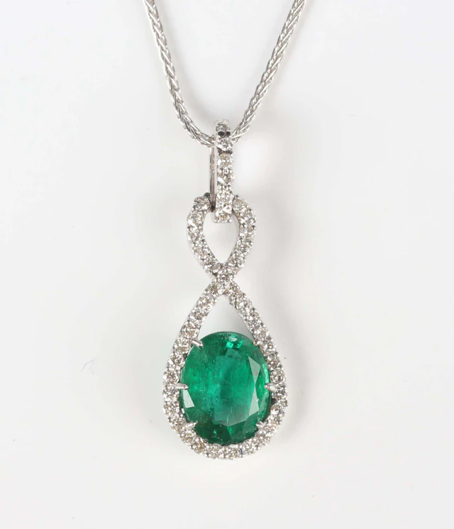 A white gold, emerald and diamond pendant, claw set with the oval