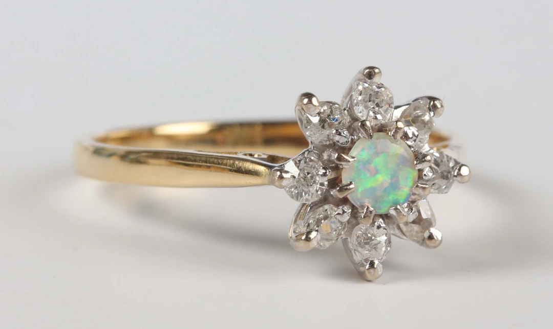 A gold, opal and diamond cluster ring, claw set with a circular opal
