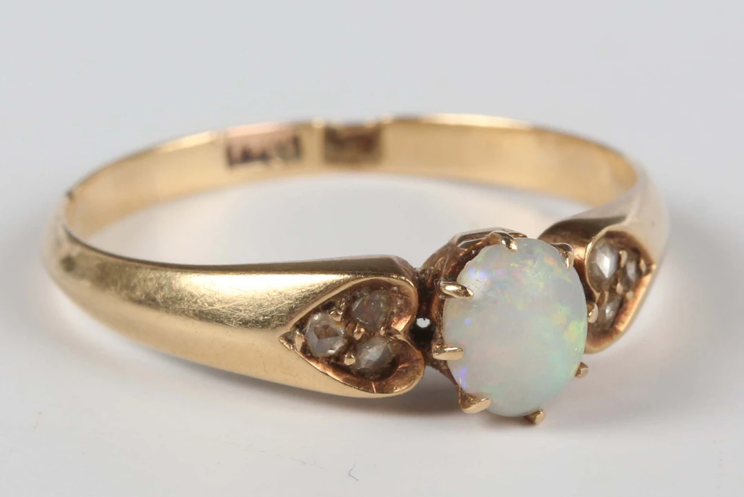 A gold, opal and diamond ring, claw set with the oval opal between