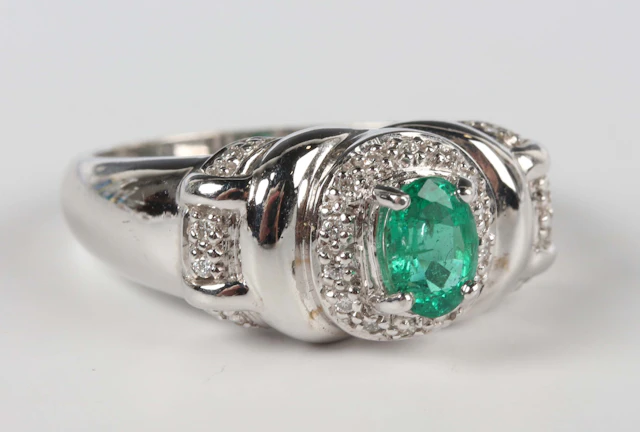An 18ct white gold, emerald and diamond ring, claw set with the oval