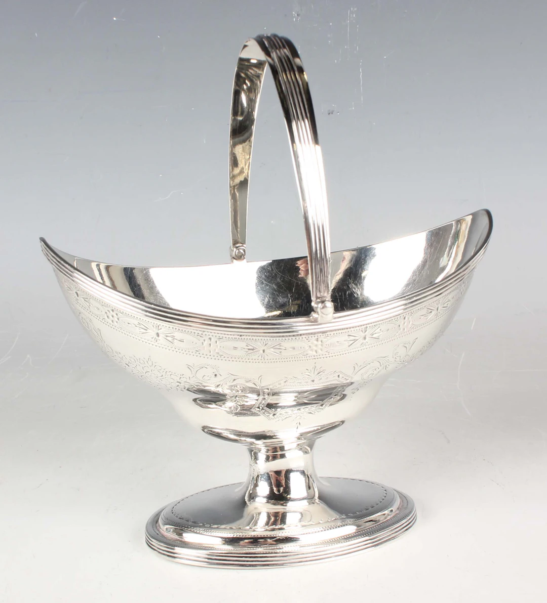 A George III silver sugar basket of oval ogee form with reeded swing