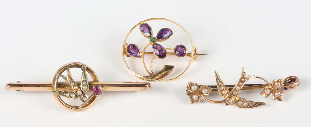 A gold and seed pearl brooch, designed a swallow between two trefoil