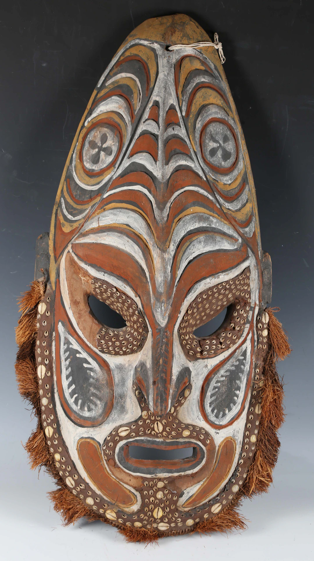 A large Papua New Guinea carved wooden mask with inset cowrie shells