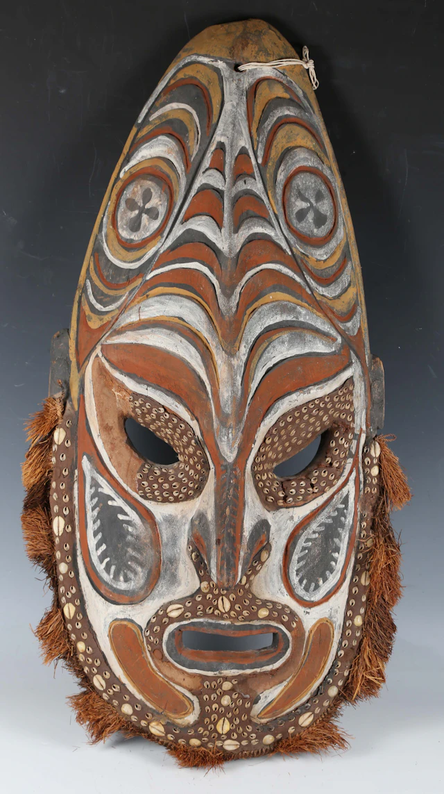 A large Papua New Guinea carved wooden mask with inset cowrie shells