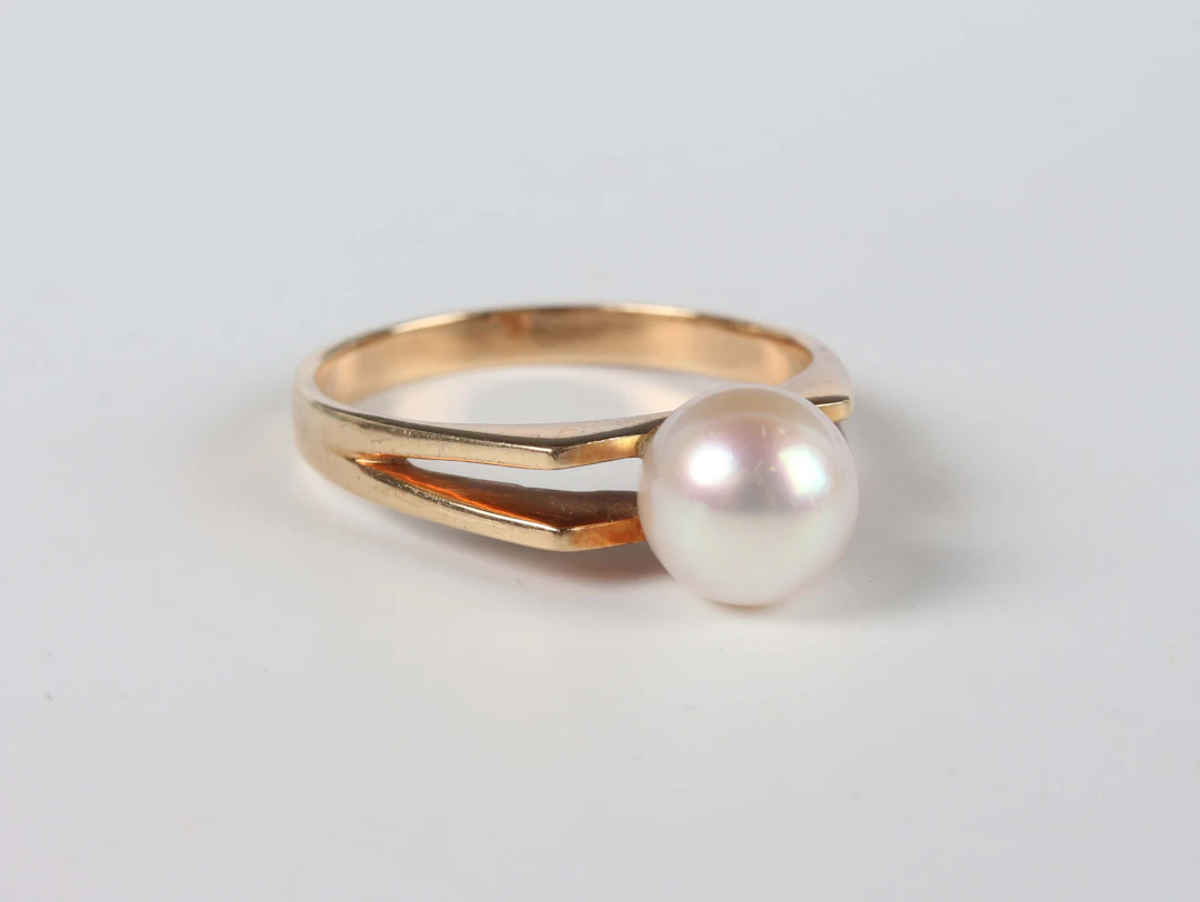 A gold ring, mounted with a single cultured pearl between split shoulders