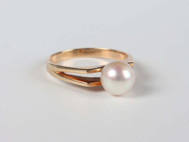 A gold ring, mounted with a single cultured pearl between split shoulders