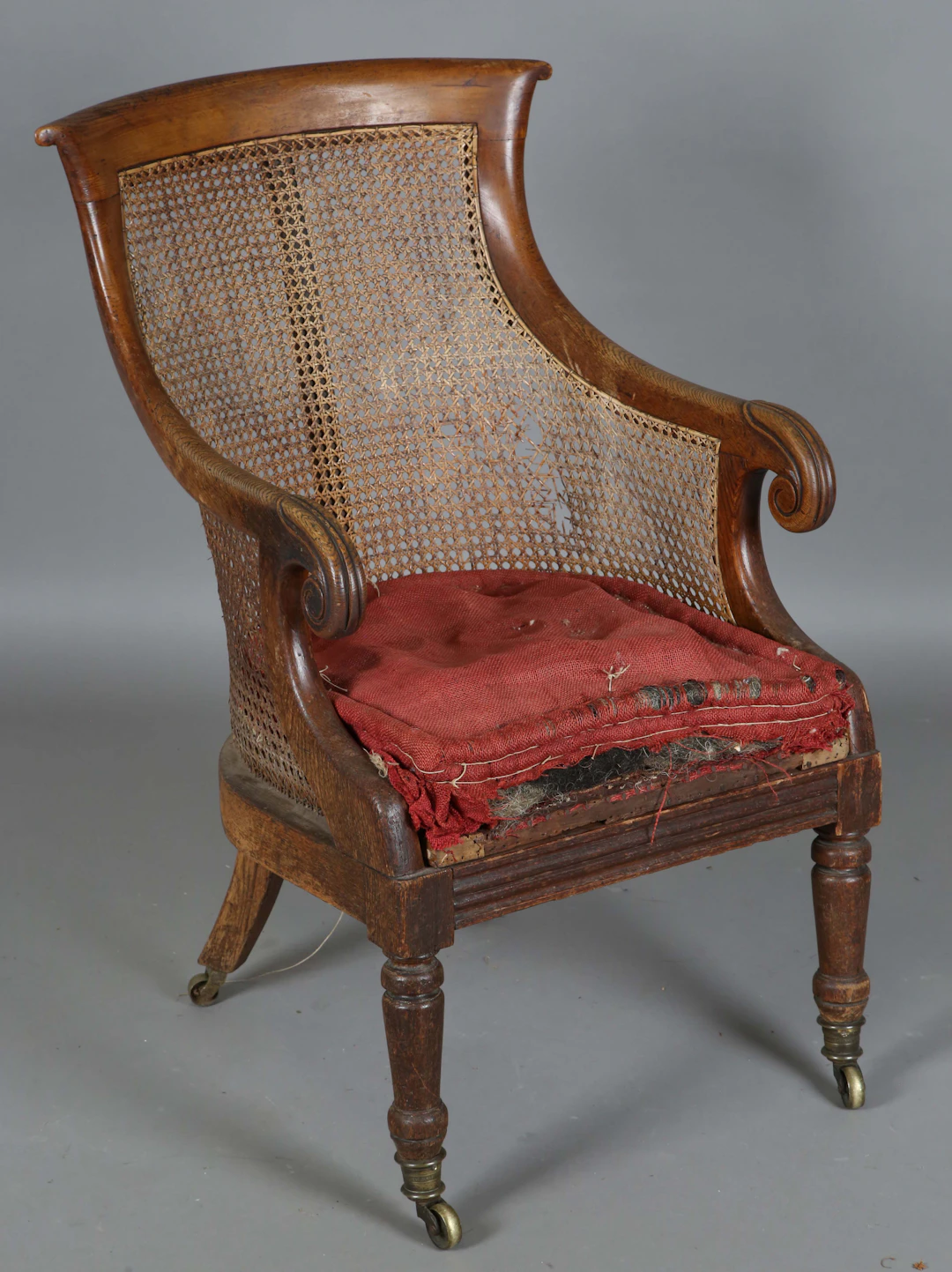 A Regency oak framed bergère library armchair, the shaped back with