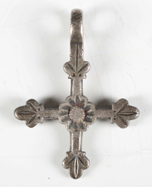 A medieval white metal cross pendant with central flowerhead and suspension