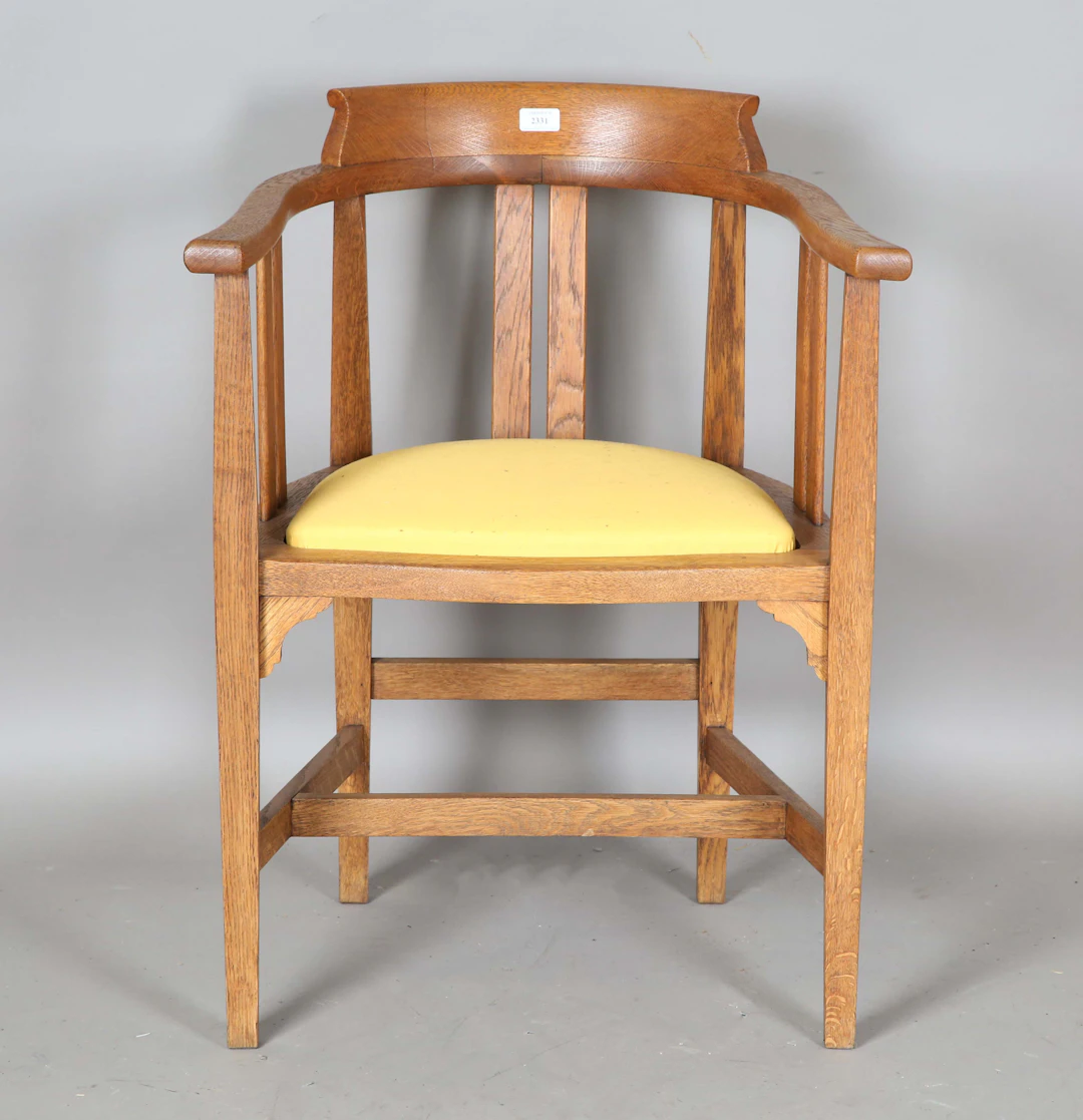 An early 20th century Arts and Crafts oak framed tub back elbow chair