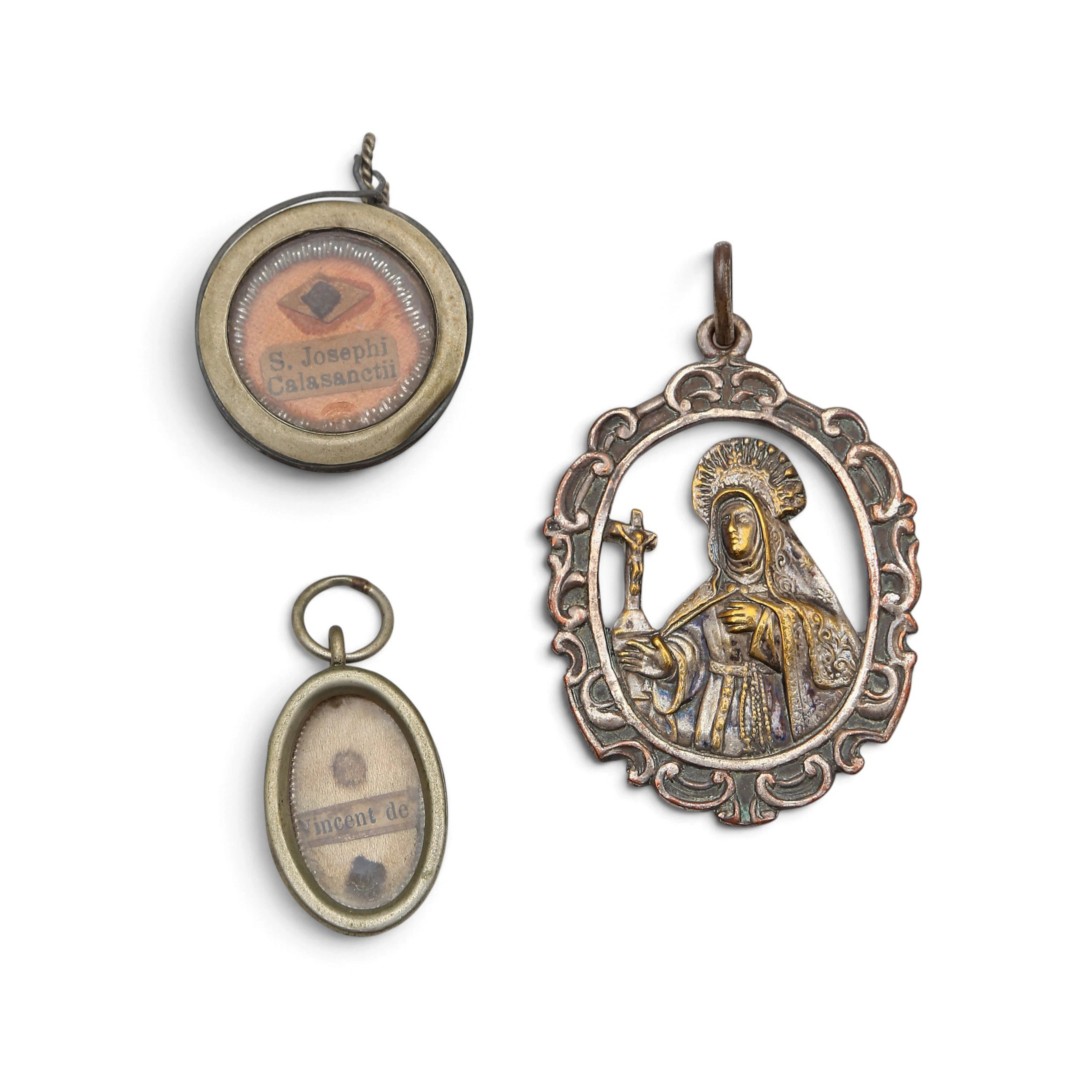 Two reliquary pendants and a Saint Teresa medal in silvery metal, 19th Century.