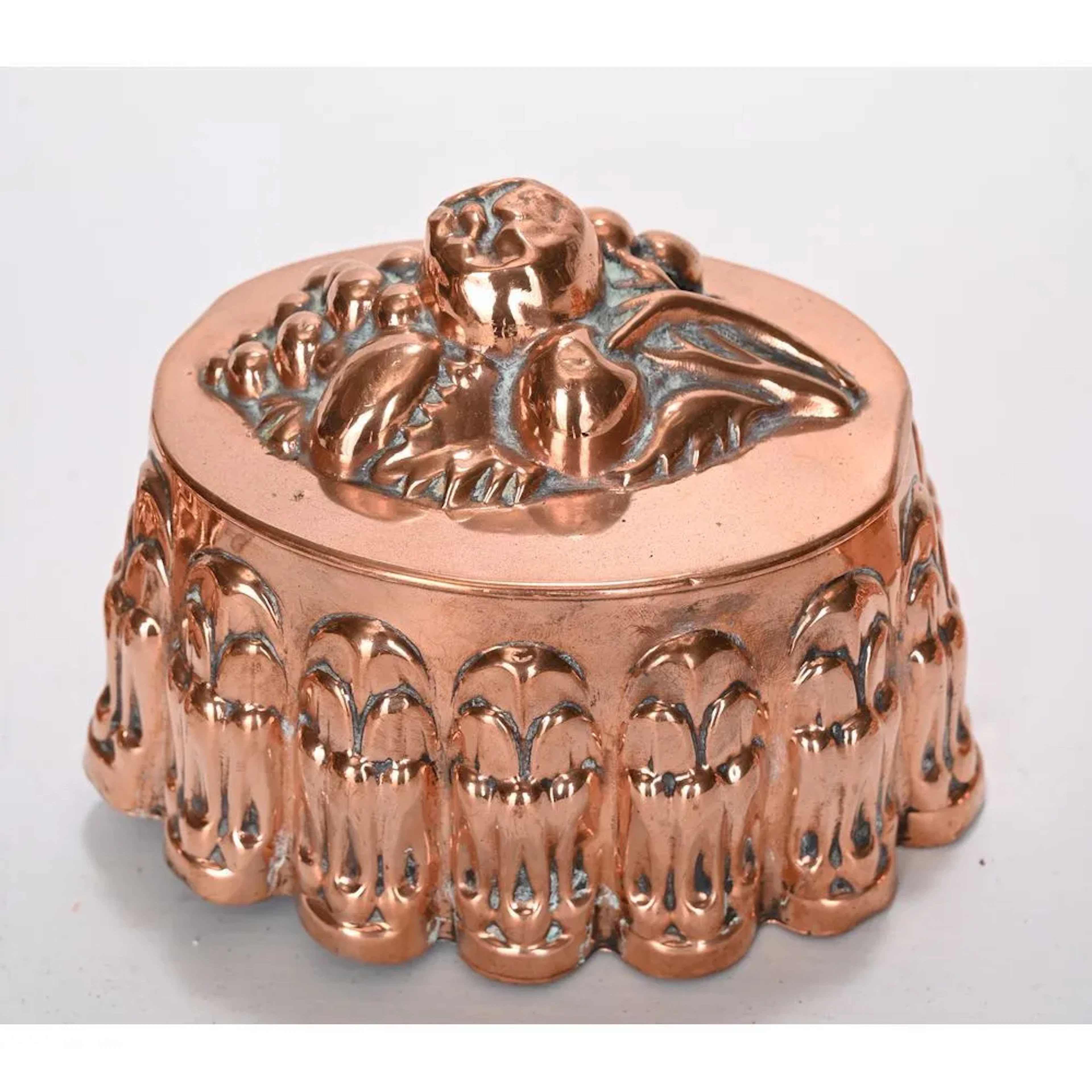 Oval-shaped copper cake pan with a fruit design on the top. Hanging