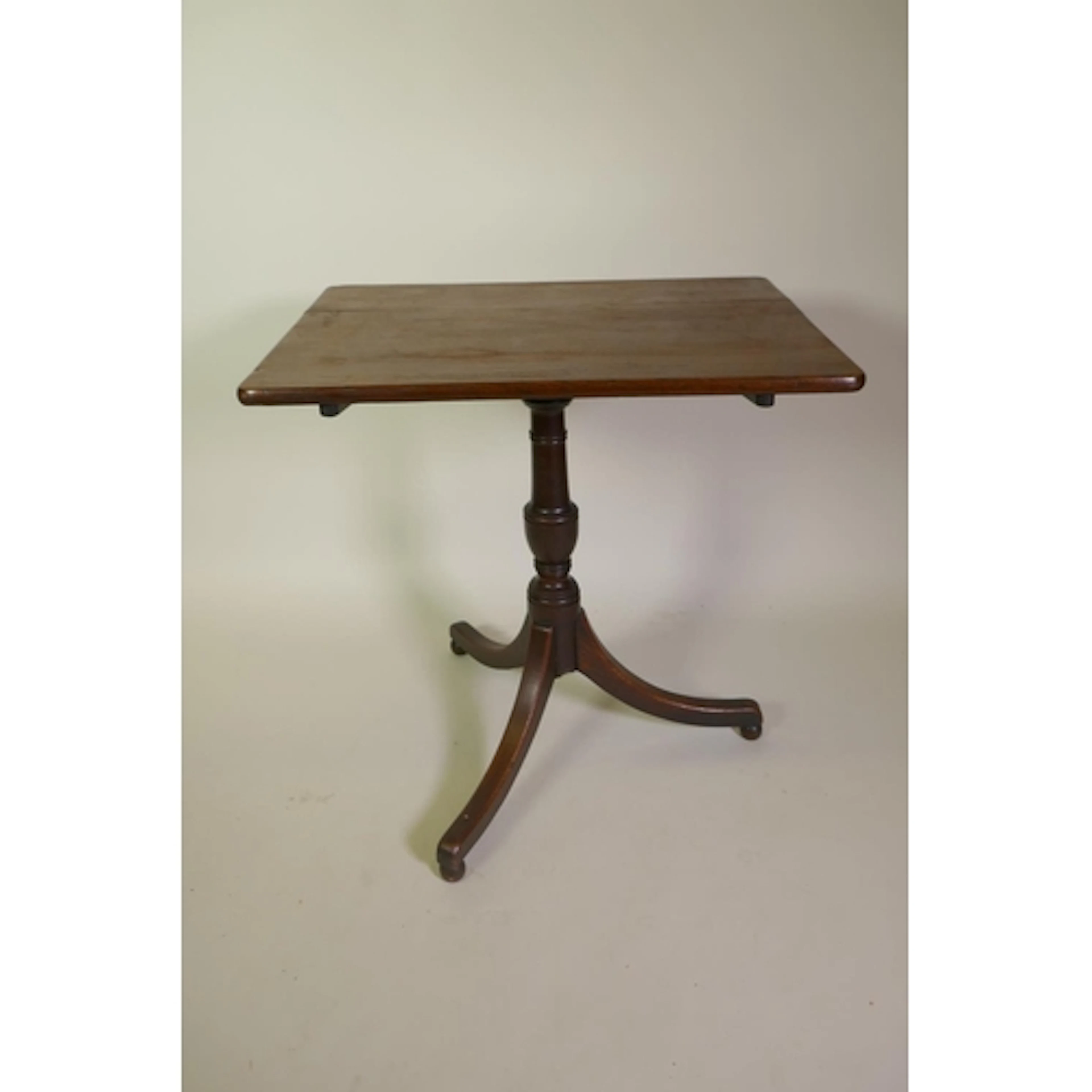 A Georgian oak tilt top table on a turned column with tripod...