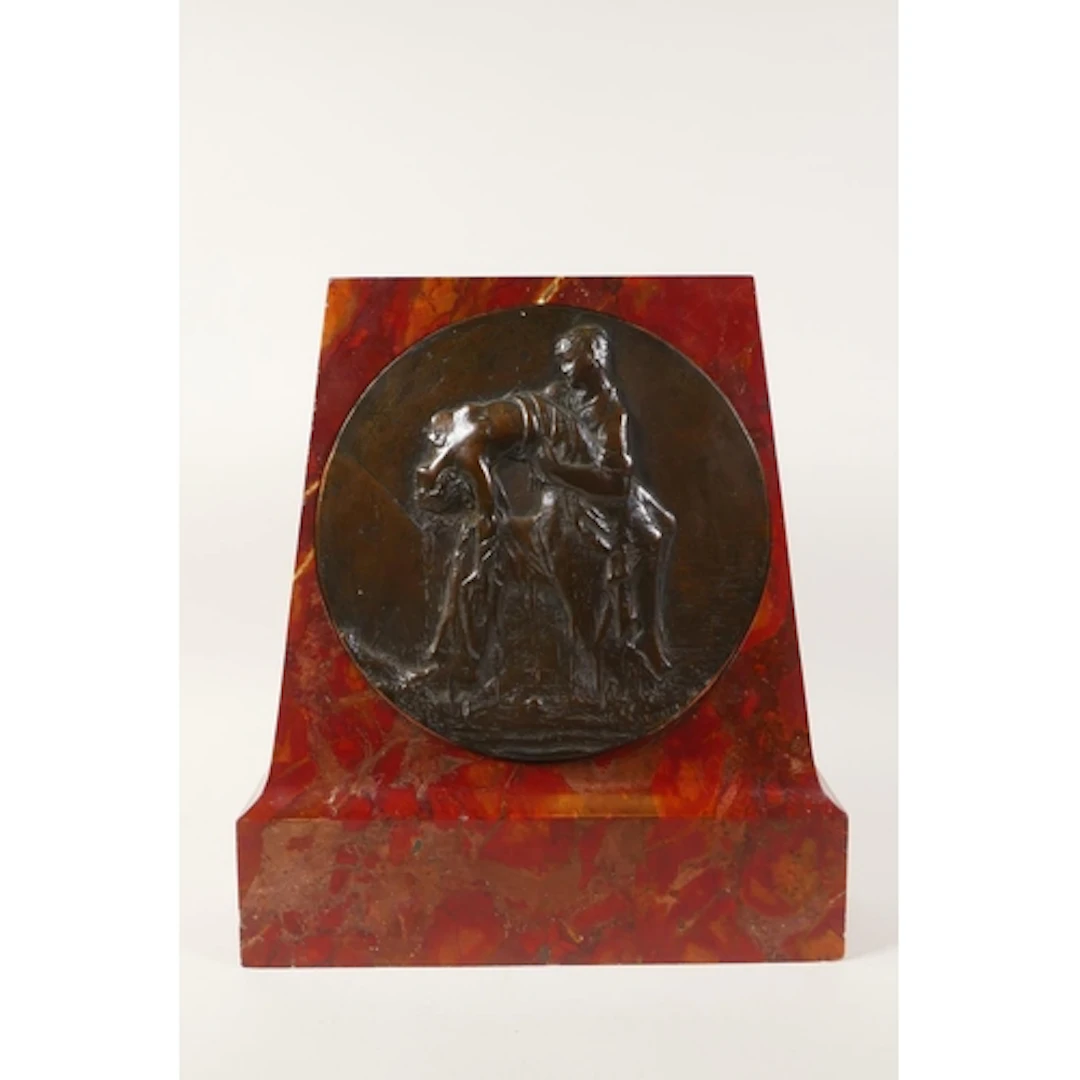An early C20th bronzed relief plaque depicting a figure crad...