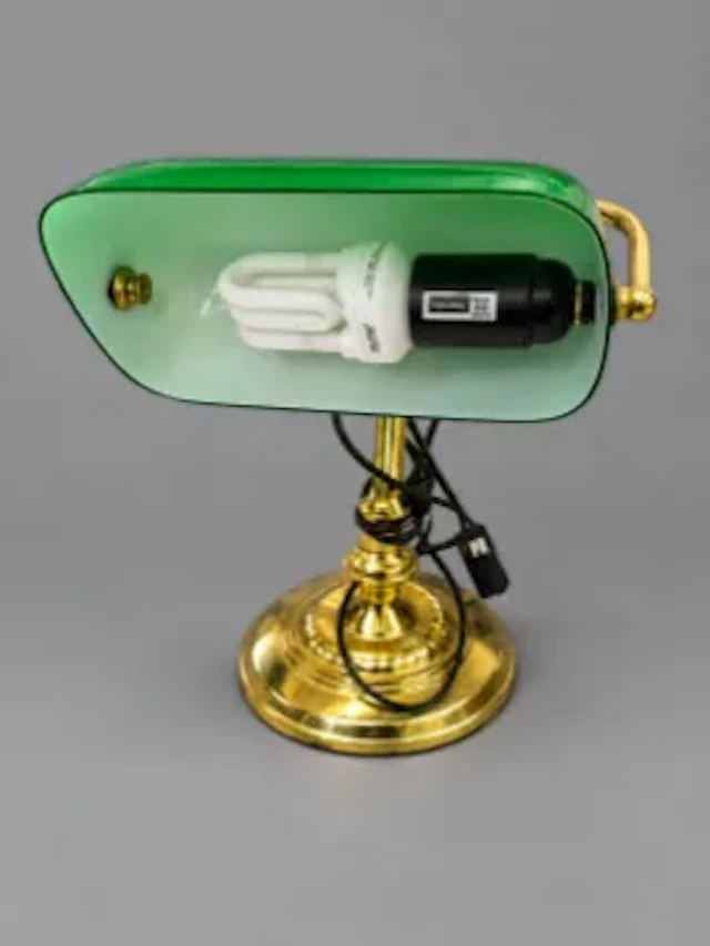 A modern desk/bankers lamp with green glass shade and brass base and frame.