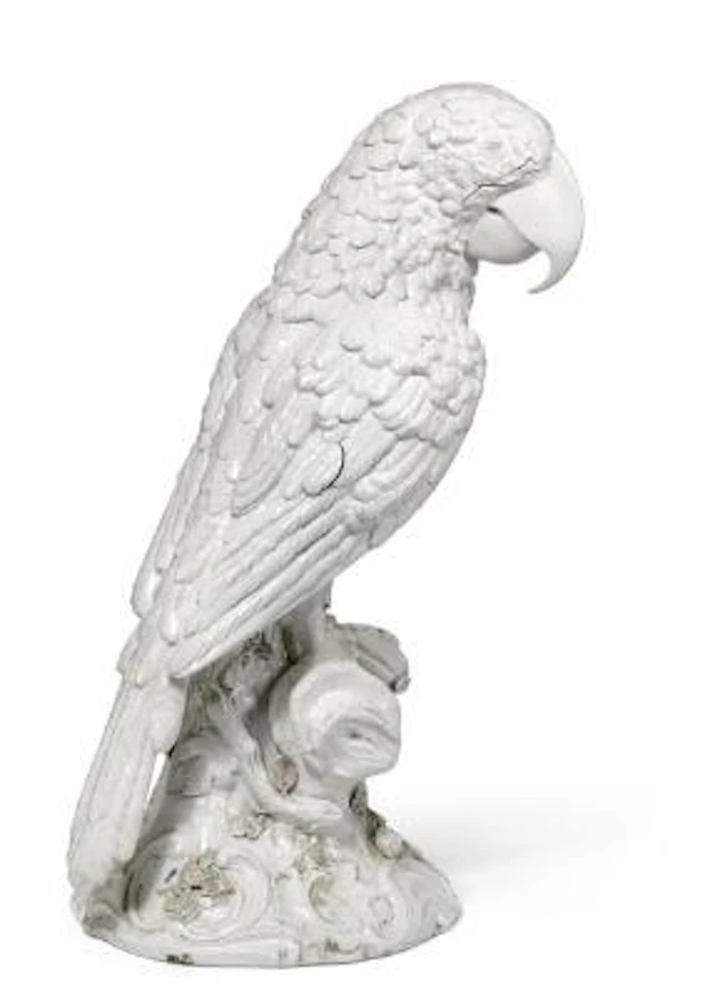 A large white glazed porcelain parrot modelled seated on wooden stump.