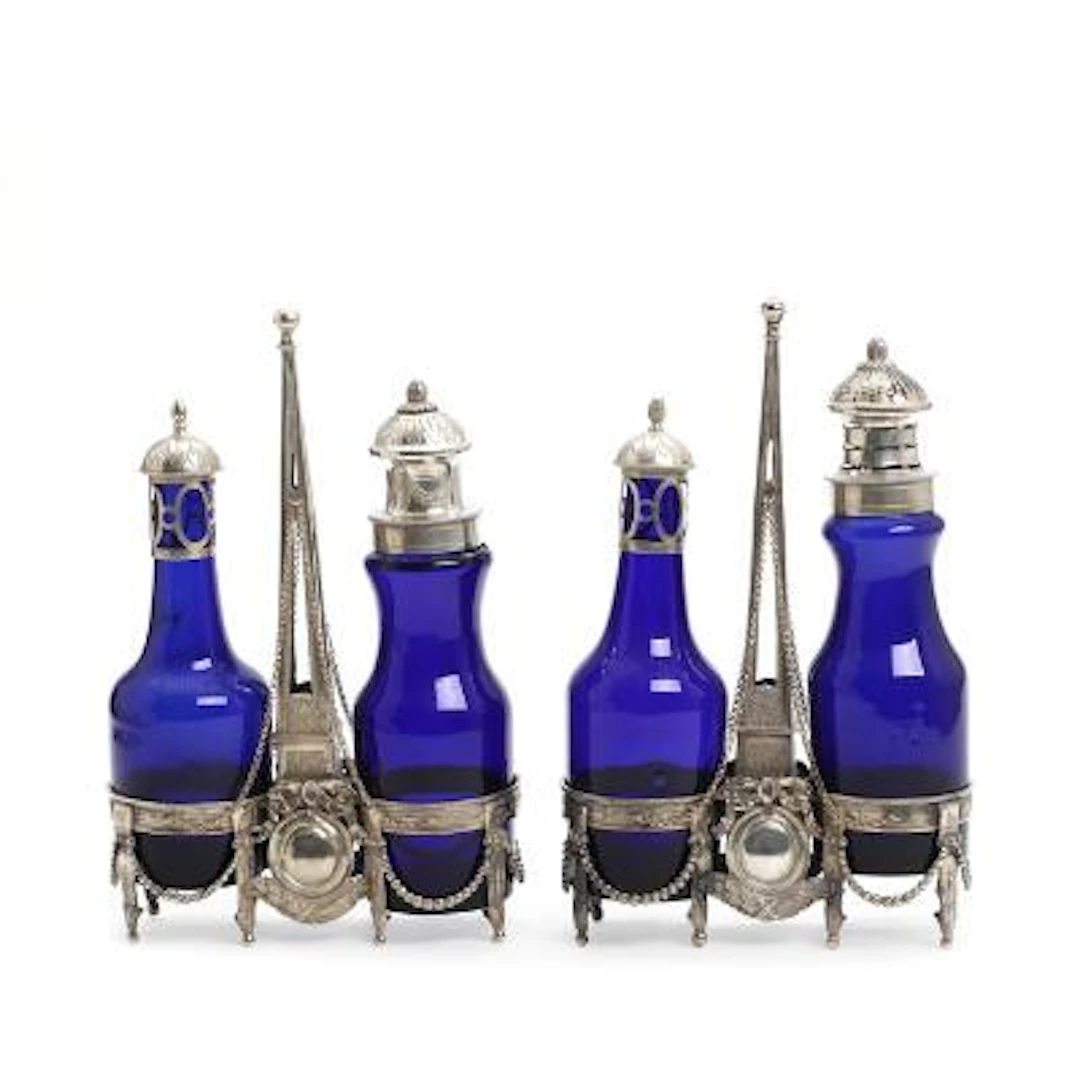 A pair of silver oil and vinegar sets, each with two blue glass bottles.