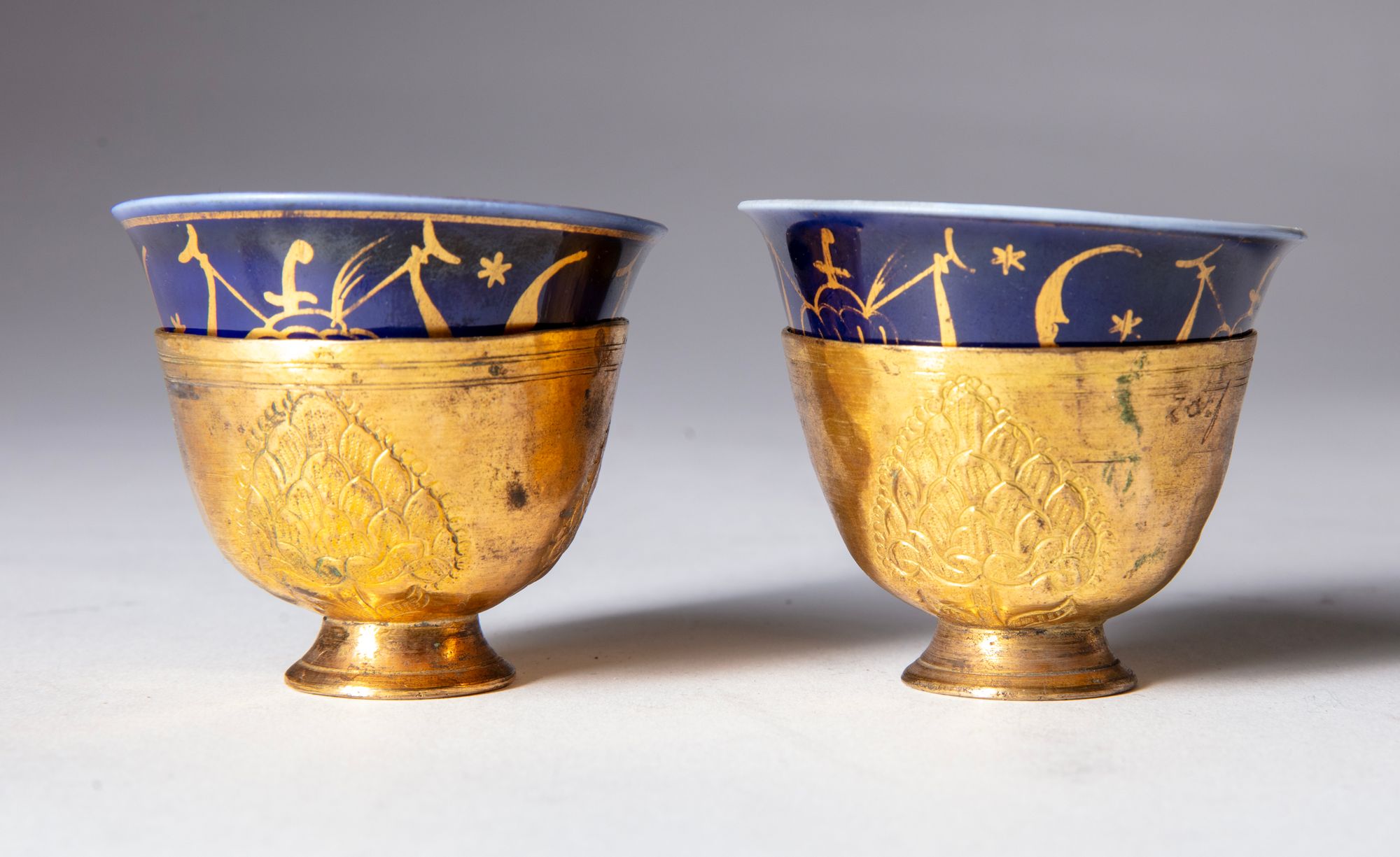 TWO OTTOMAN GILDED TOMBAK ZARF HOLDERS, WITH ORIGINAL PORCELAIN ZARFS