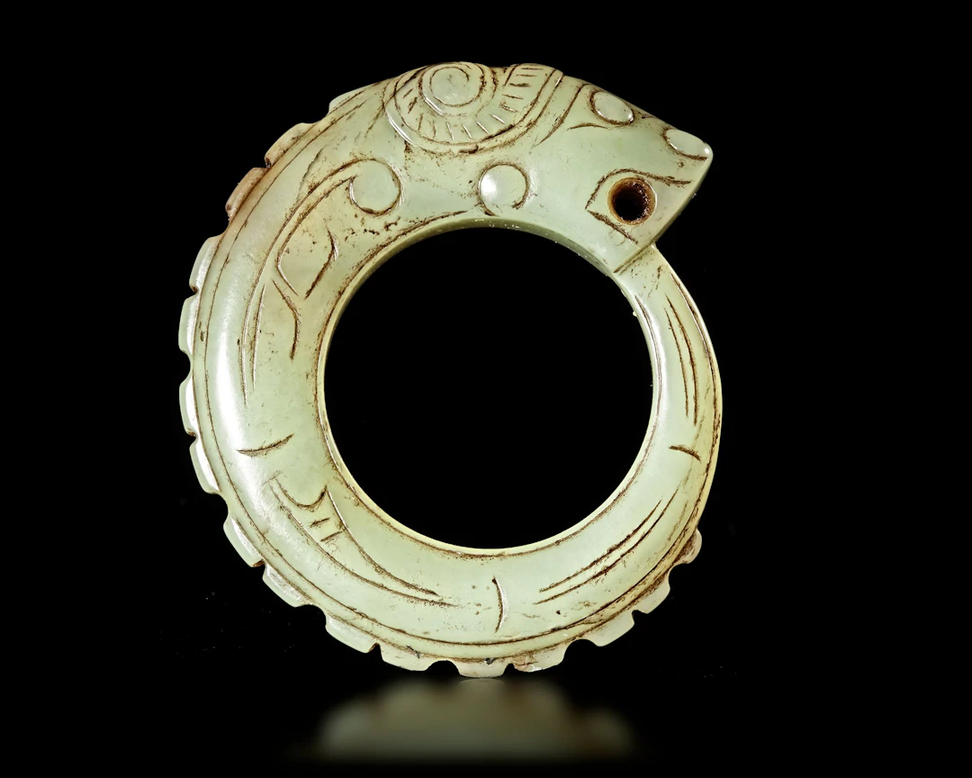 A LIGHT GREEN JADE OUROBOROS DRAGON PENDANT, CHINA, WESTERN ZHOU DYNASTY